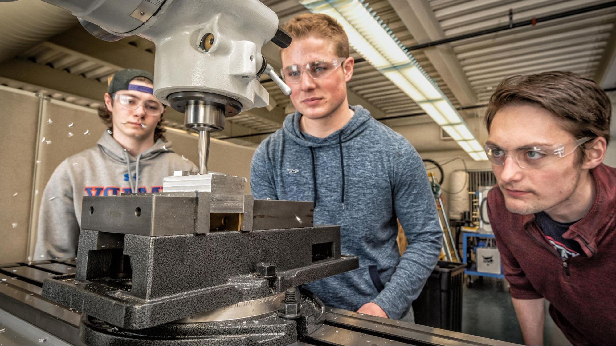 Three engineering students work together to operate a drill saw